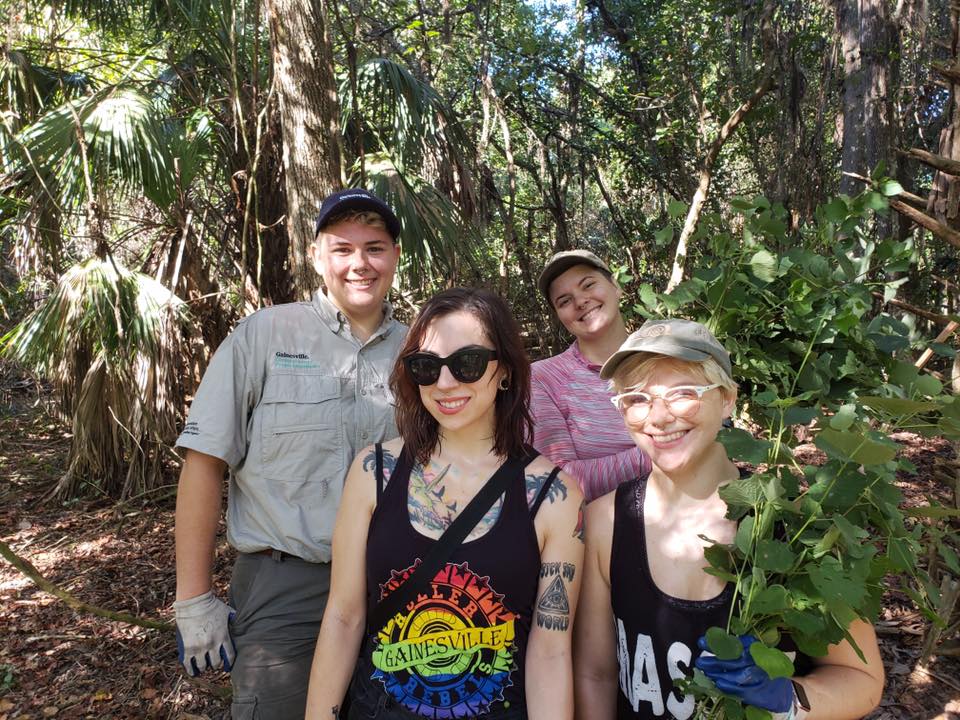 Caro, Lyka, Gnarly, and Toast pose in a park with some invasive plants