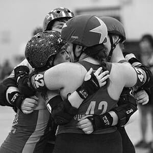 roller derby teammates embrace at a Swamp City Sirens bout. Picture is in black and white